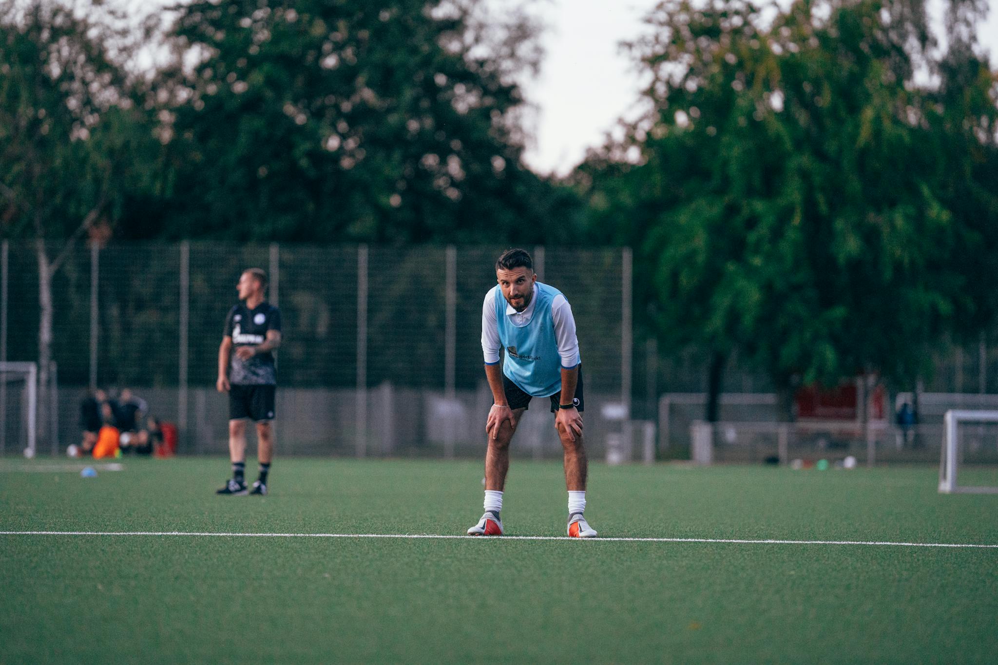 Male soccer player in uniform standing in field and leaning on hands during training in grassy field