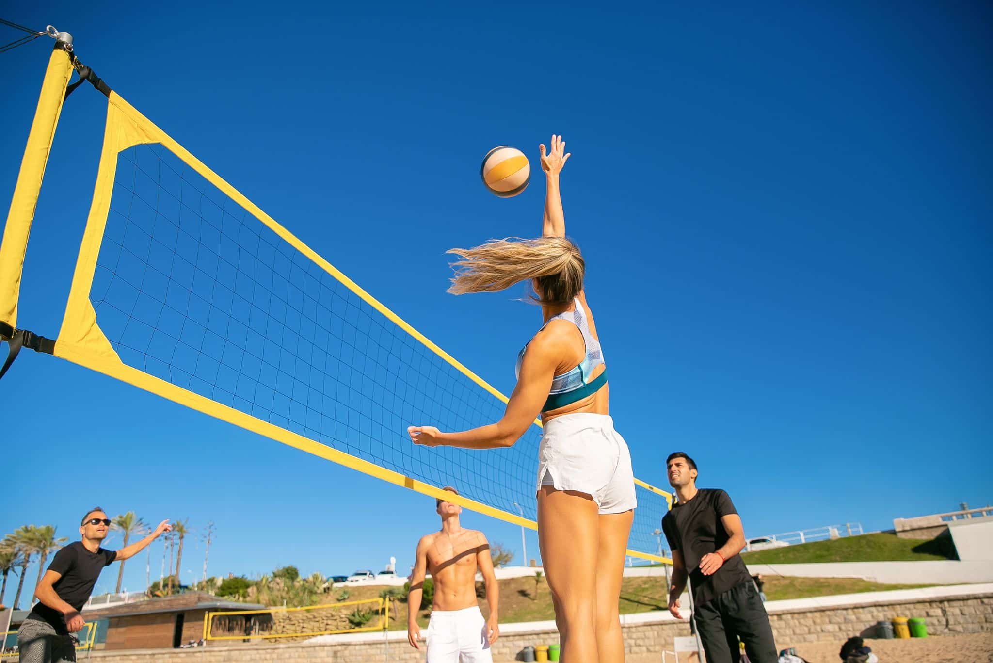 Group of adults playing beach volleyball under a bright blue sky.