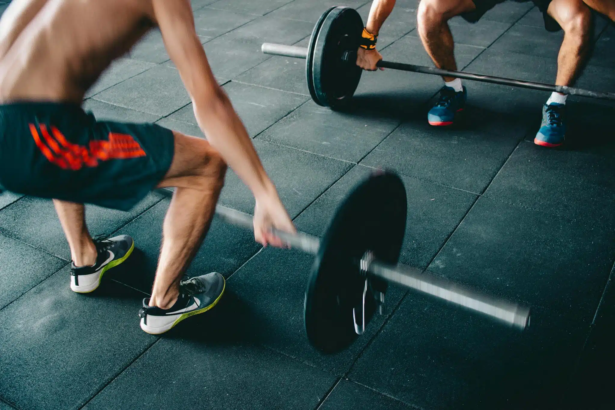 Two men lifting barbells showing strength and effort in a gym setting.