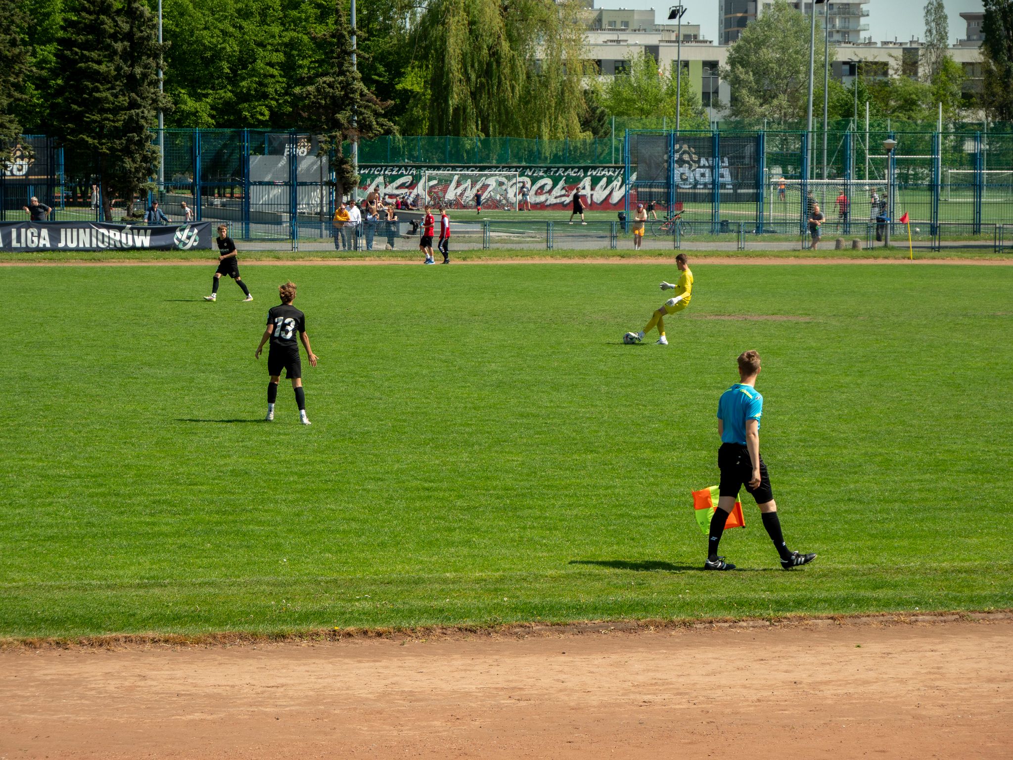 Youth soccer game at WrocĆaw sports field on a sunny day with players and referee in action.