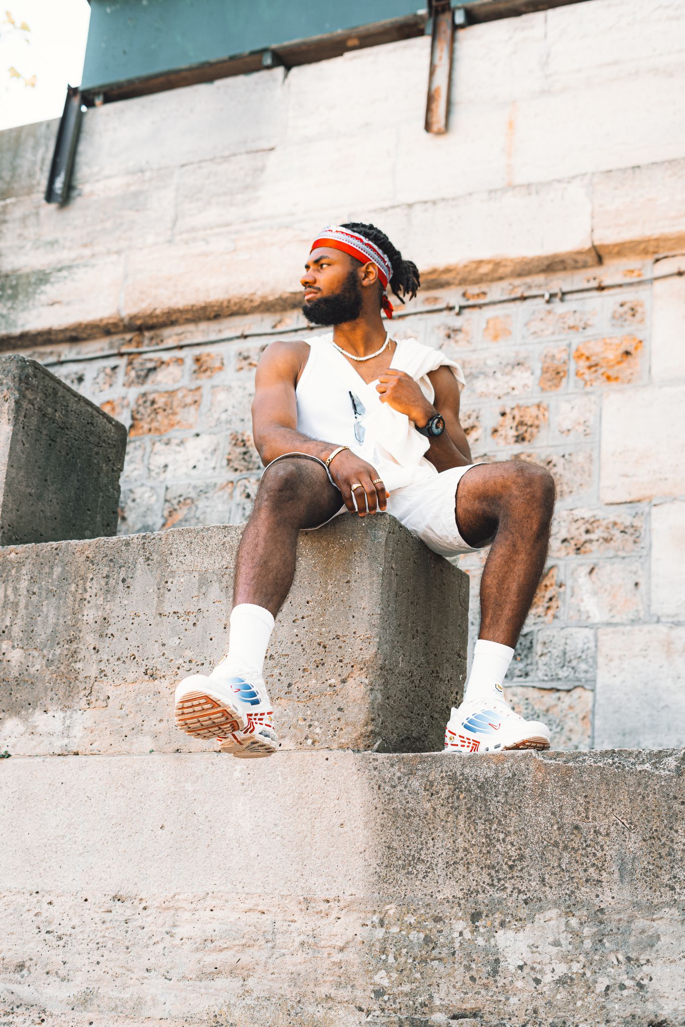 Stylish man with beard poses confidently in trendy streetwear, sitting on urban concrete steps.