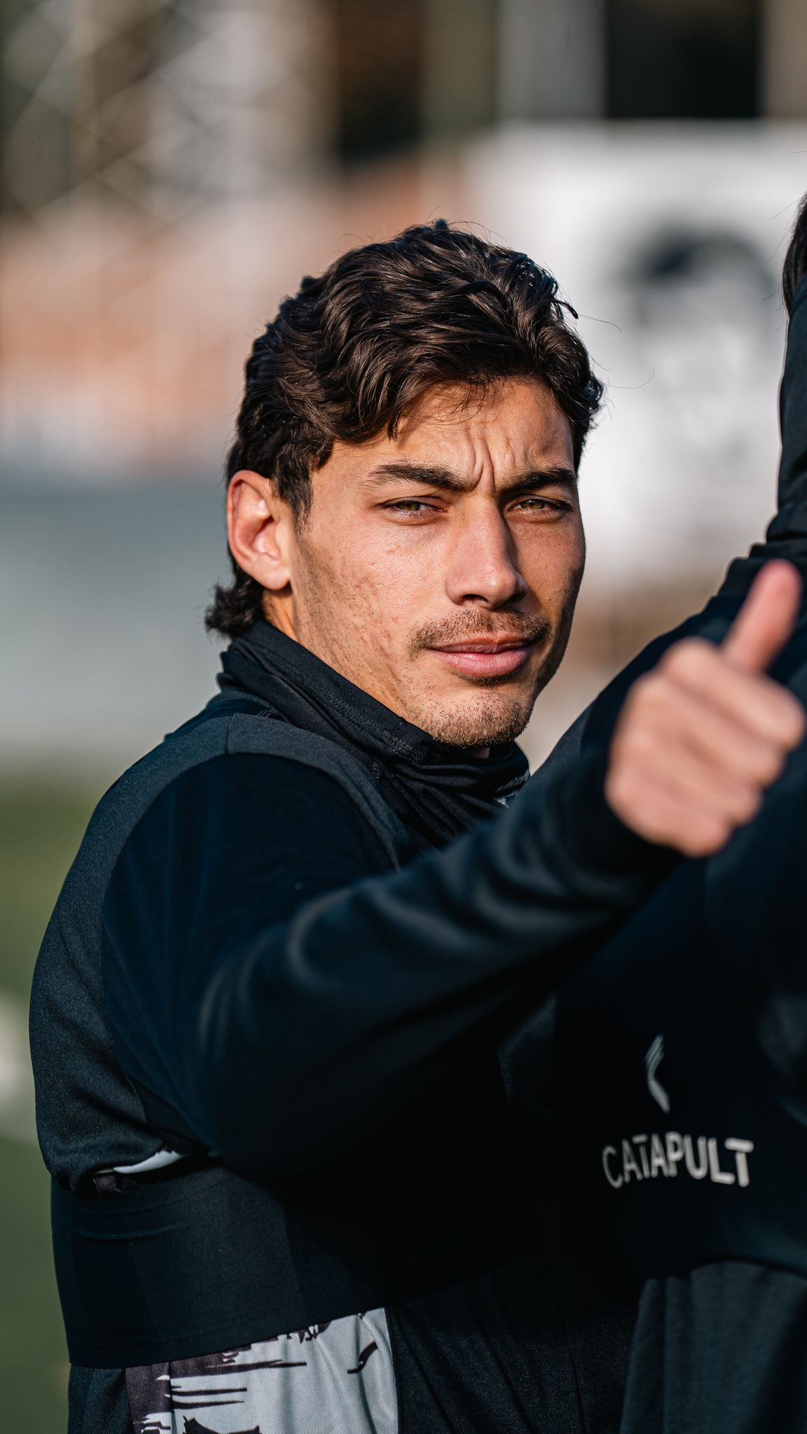 A young male athlete gives a thumbs up gesture outdoors, showcasing confidence and positivity.